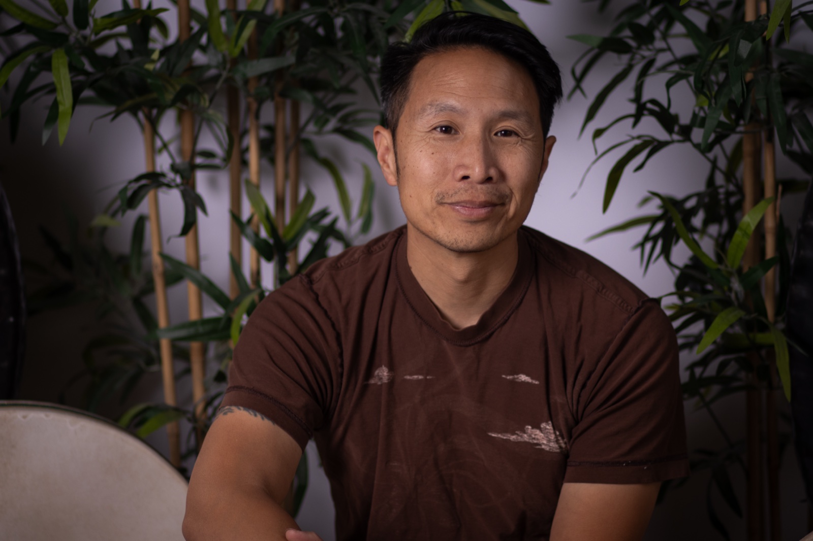Marcus Fung, sound therapist and facilitator, with a frame drum among bamboo plants