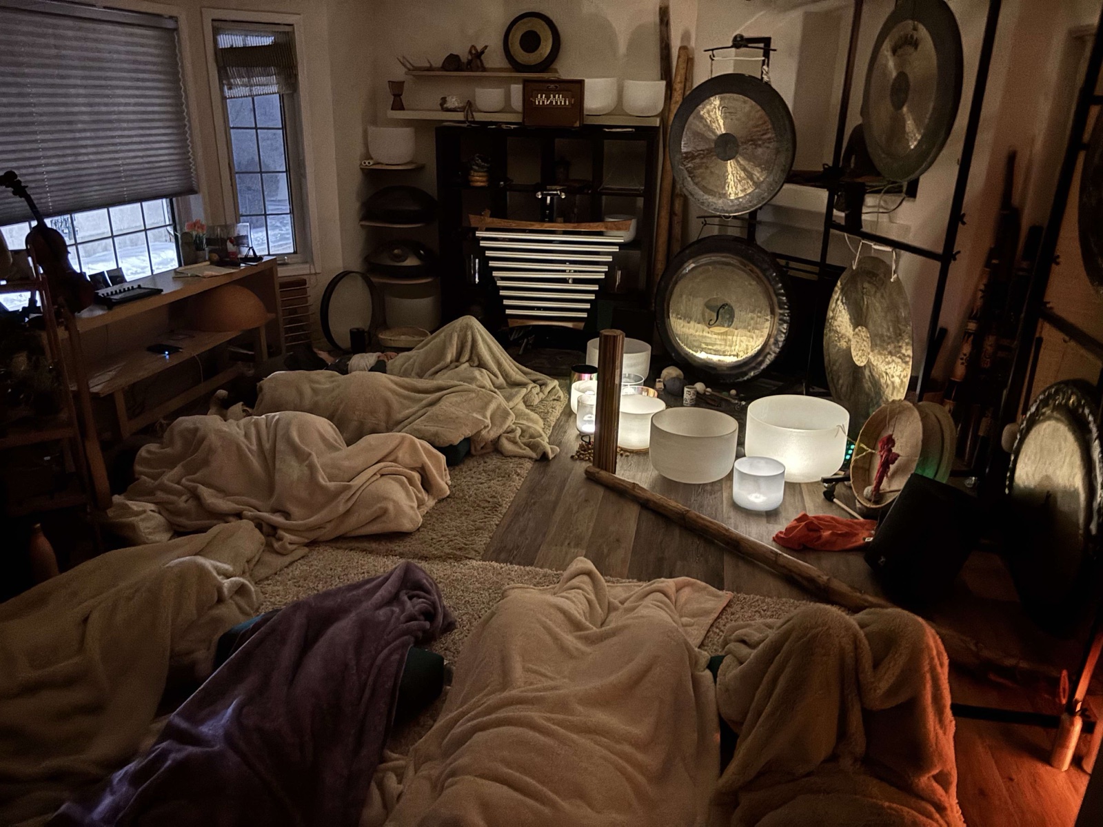 Community sound bath — participants resting under blankets among gongs and crystal bowls