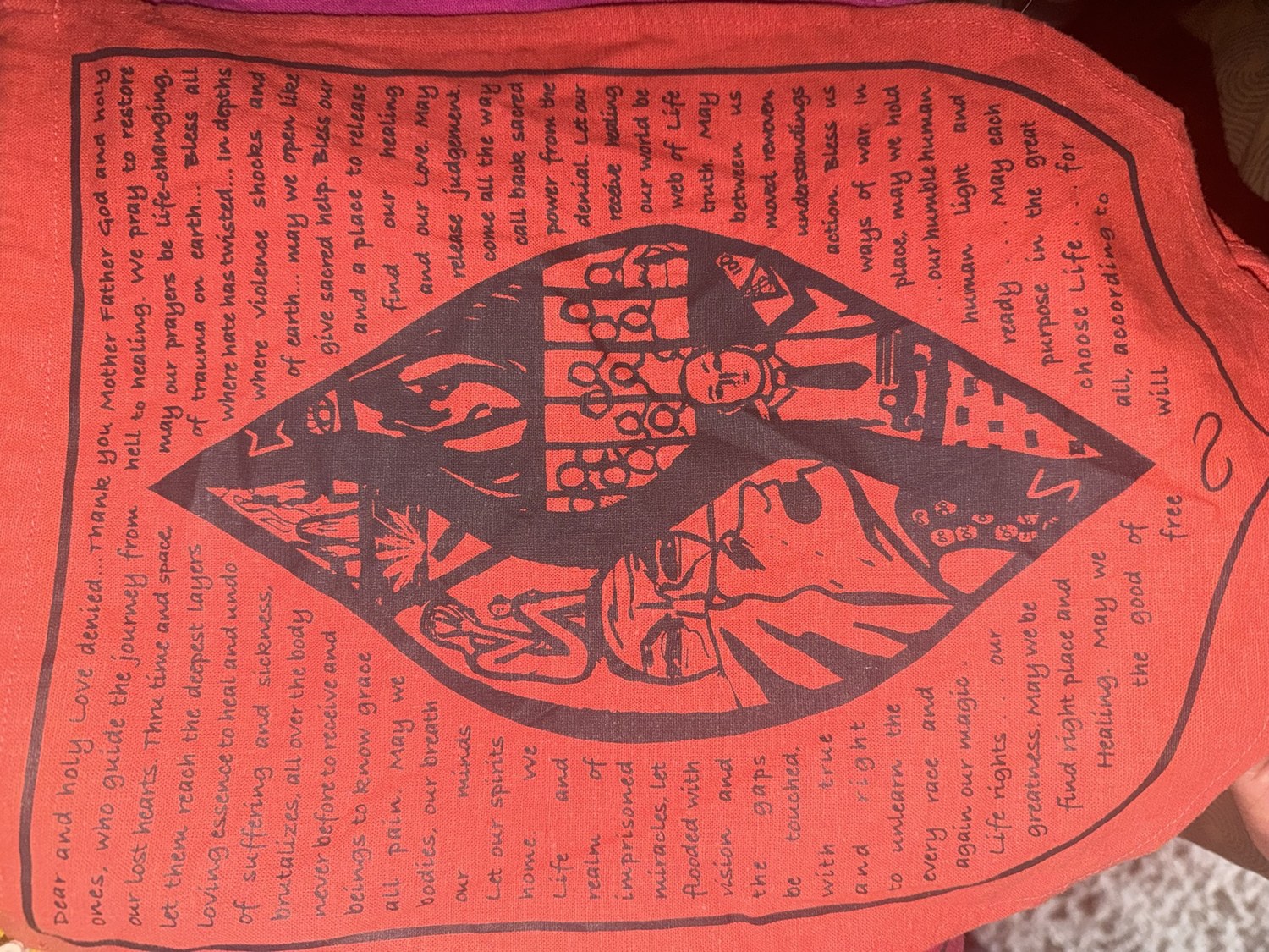 A red cloth prayer flag, hand-lettered in black ink around a central linocut — the Prayer for the Love Denied
